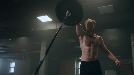 A-male-athlete-lifts-a-weight-bar-with-one-hand-in-slow-motion.-Strength-training-for-a-boxer.-The-man-is-sweating-working-out-in-the-gym-practicing-the-force-of-the-blow-with-his-hand